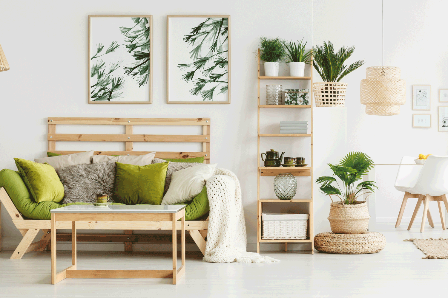 Leaves posters on white wall above green settee with pillows and blanket in spacious living room interior with plants, lime accent