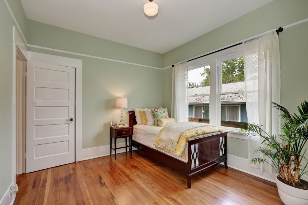 Mint green painted walls of a small cozy bedroom with wooden flooring, white door and a white casement window