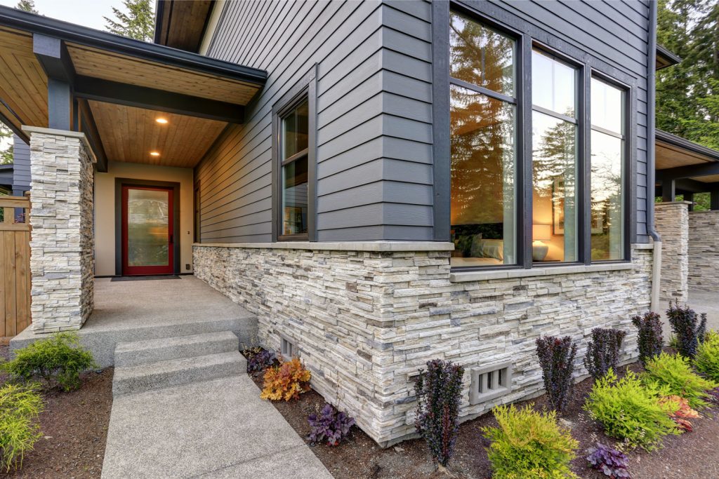 Modern contemporary house with gorgeous, gray sidings, decorative stone cladding and plants in front of the porch