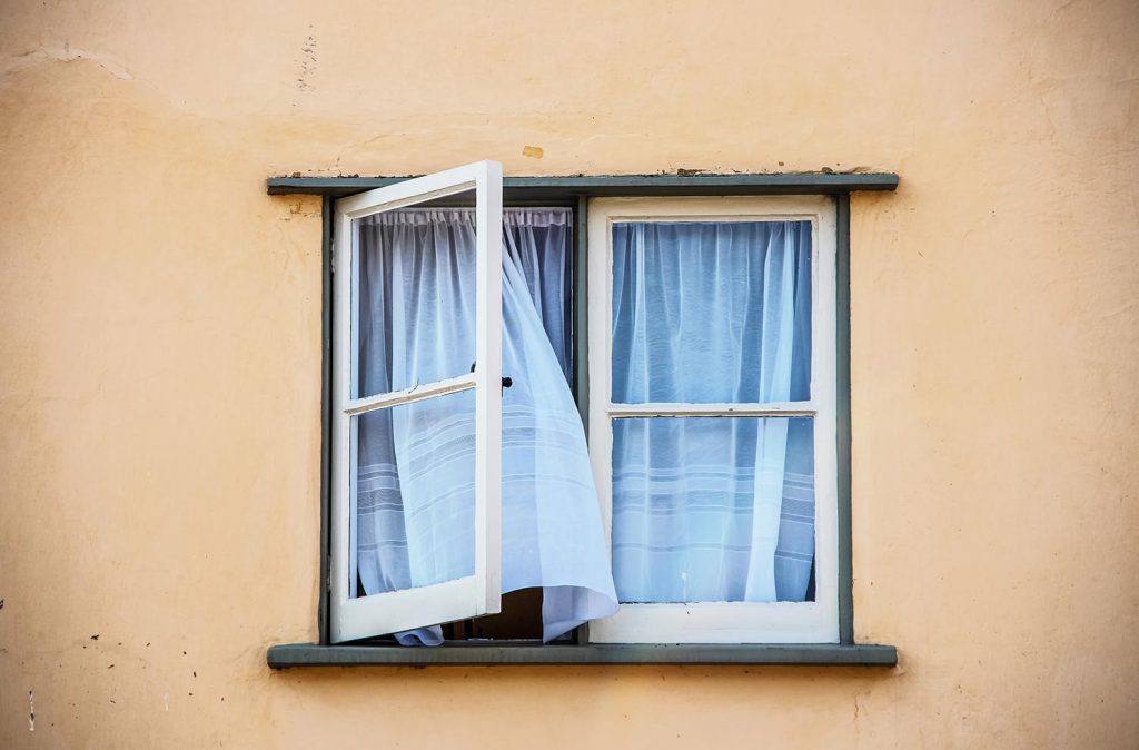 Open casement window in old stucco house with white gauze sheer curtains
