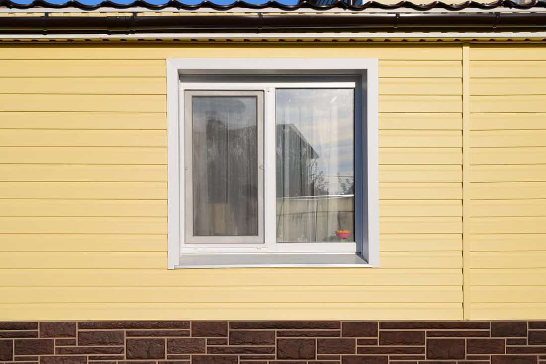 The wall of a private house with a window covered with yellow siding