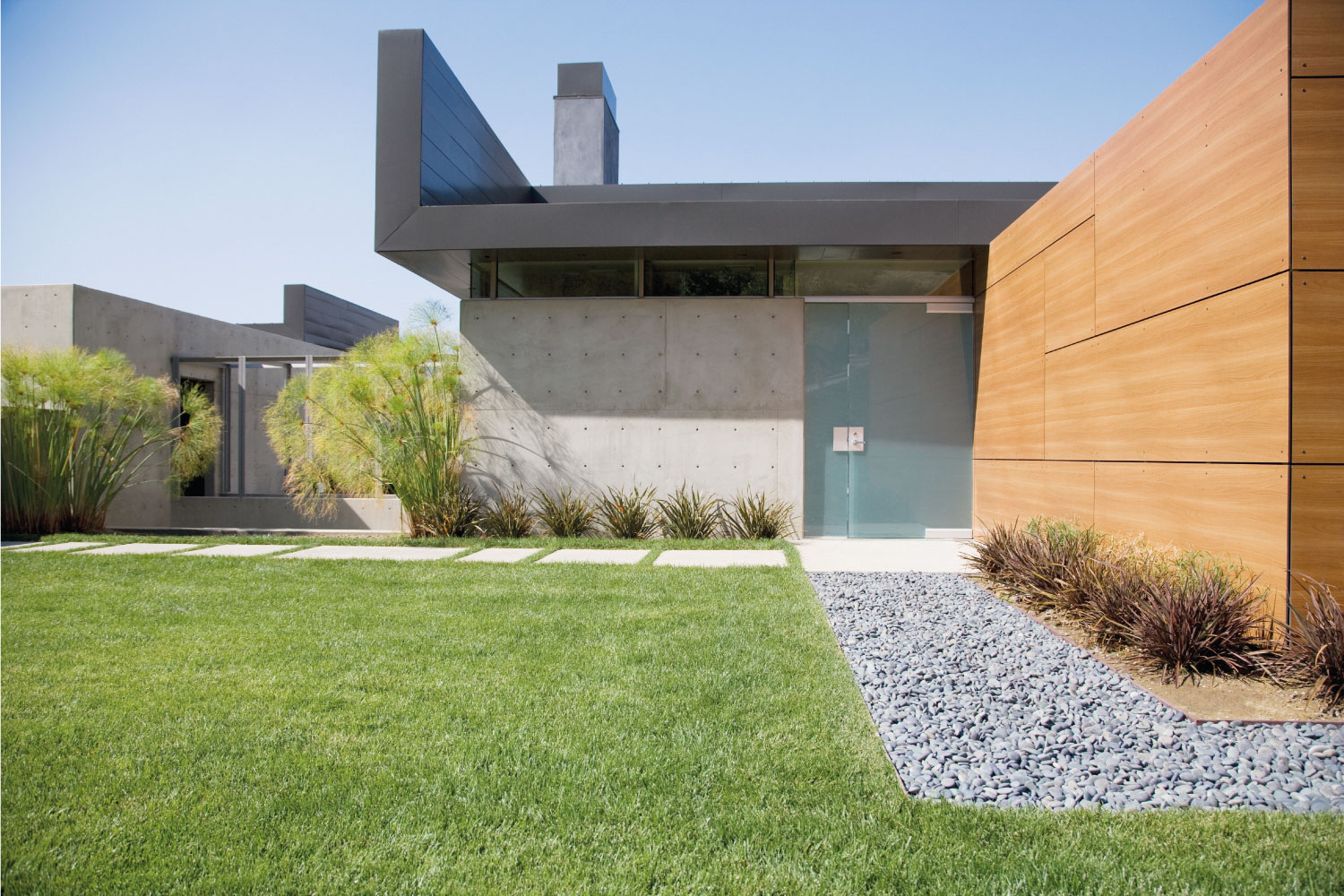 modern exterior landscape. lawn, gravel, and concrete pavers with wood panel wall