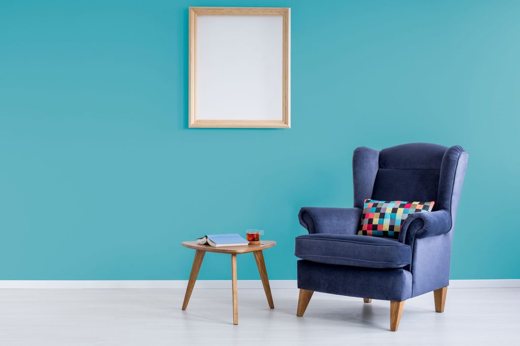 A blank canvas mounted on a teal painted wall and a dark blue accent chair