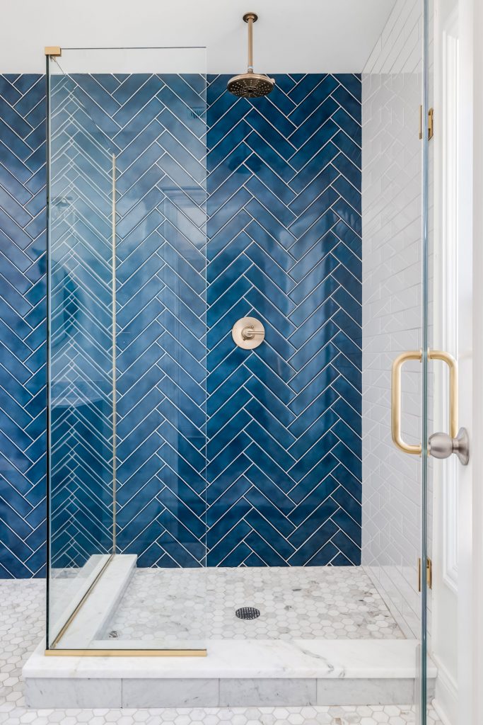 A blue single herringbone tiled shower in a luxury home with gold hardware.
