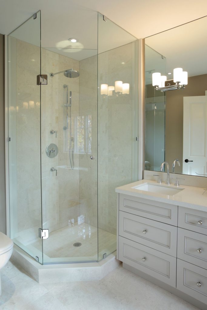 A corner glass walled shower area in a modern bathroom and a light gray colored vanity cabinet