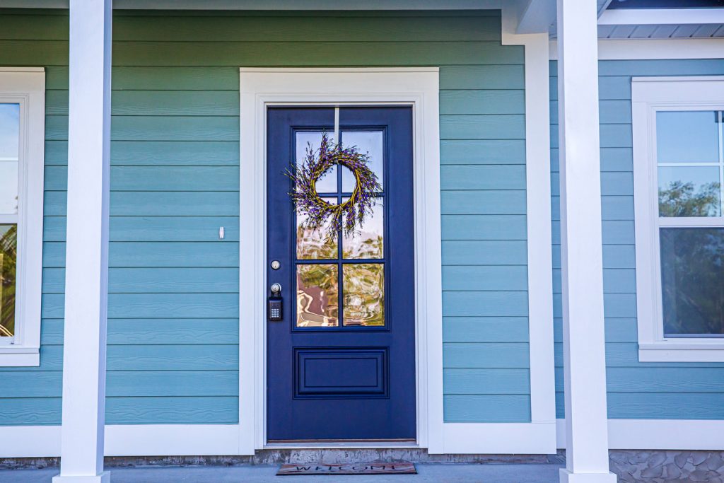 A gorgeous front porch with wooden sidings, blue front door with a decorative wreath and white trims