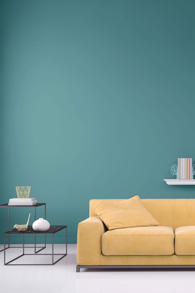 A teal painted wall with a yellow sofa