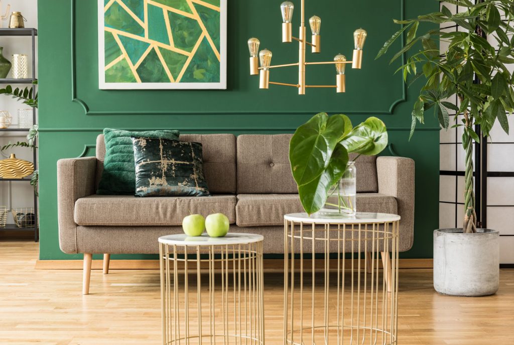 Elegant green and gold living room with comfortable brown sofa, coffee tables and golden chandelier