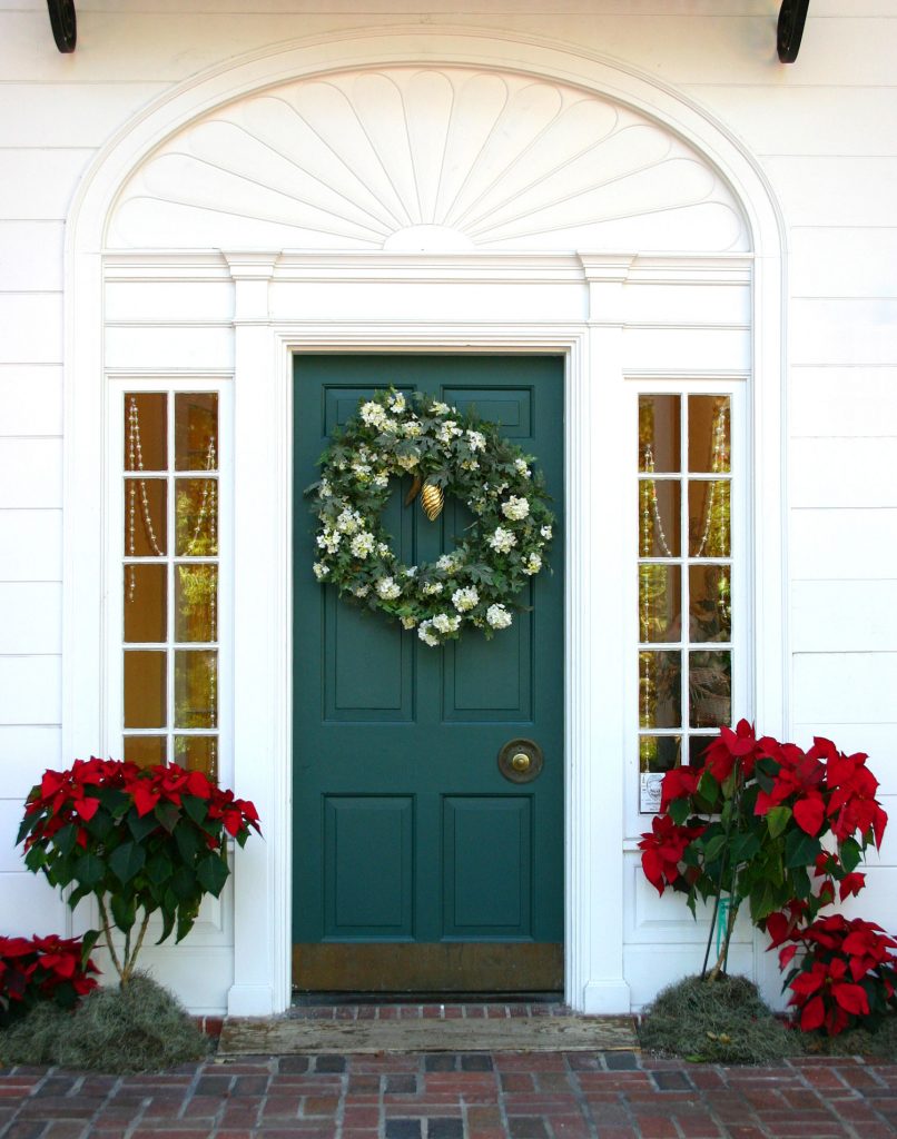 Green door decorated for the winter holidays. Poinsettias and wreath.