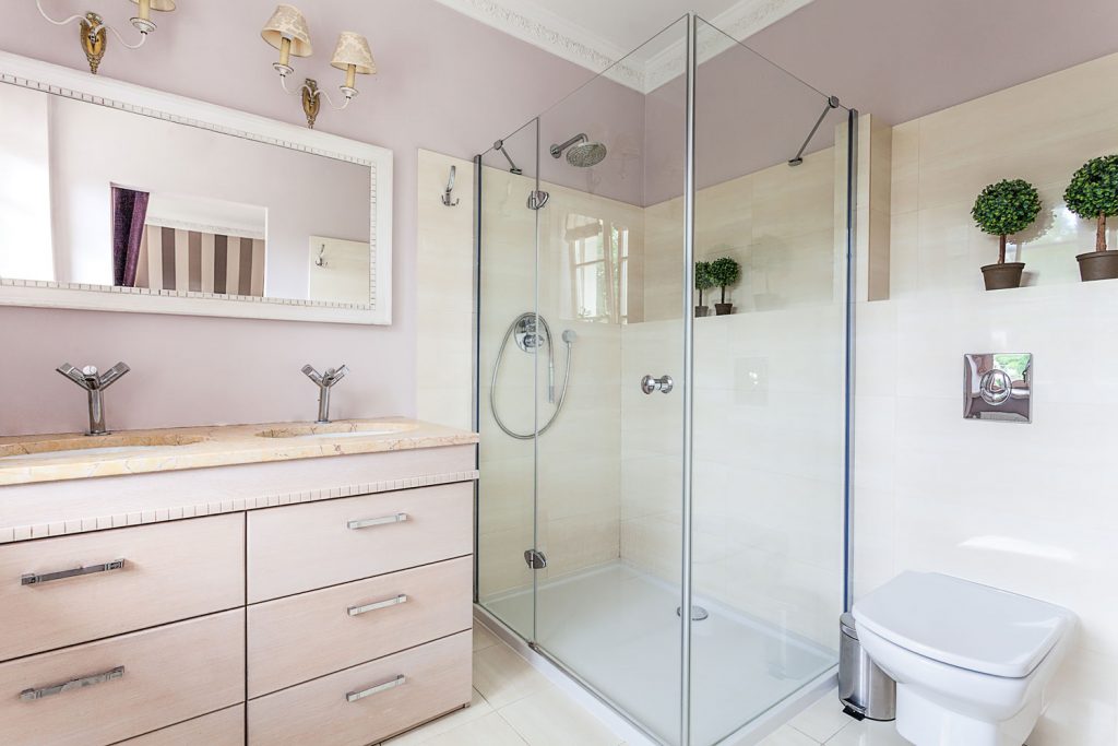 Interior of a modern bathroom with a glass shower wall, pink colored cabinets and small plants on the wall