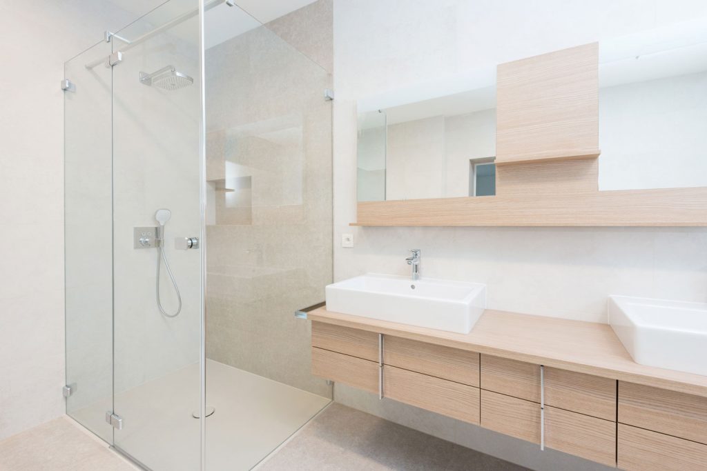 Interior of an empty modern bathroom with wooden paneled cabinets and a glass walled shower area