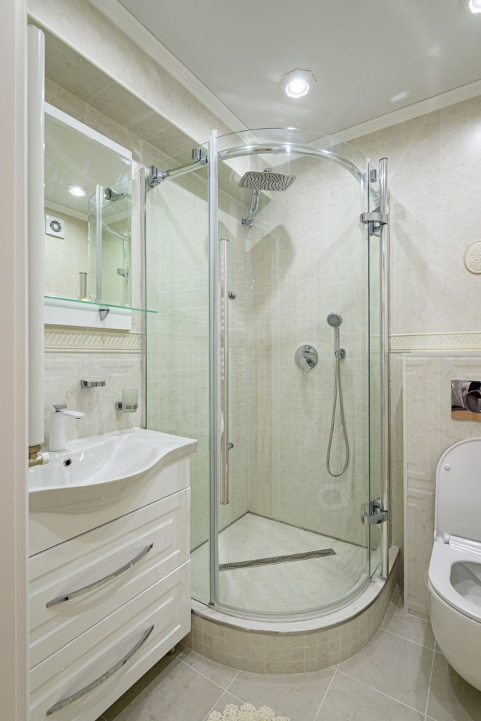Круглая угловая стеклянная душевая стена с белыми шкафами в туалетном столике