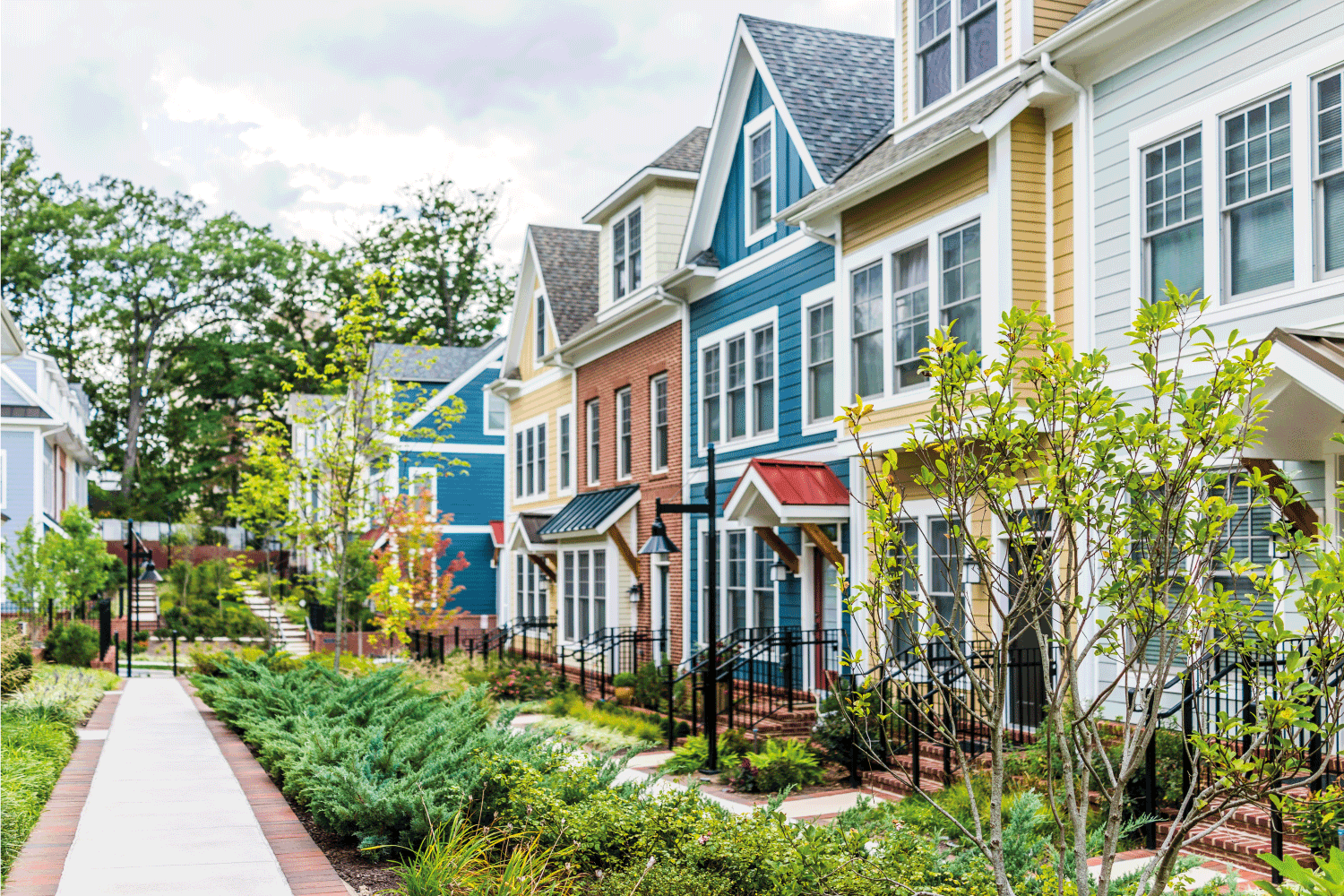 Row of colorful, red, yellow, blue, white, green painted residential townhouses, homes, houses with brick patio gardens