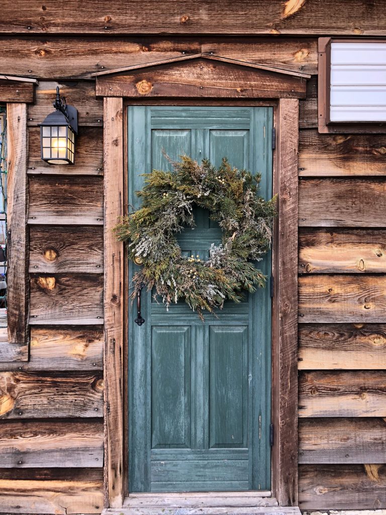 Rustic wood home with blue green front door, fresh wreath hanging on door