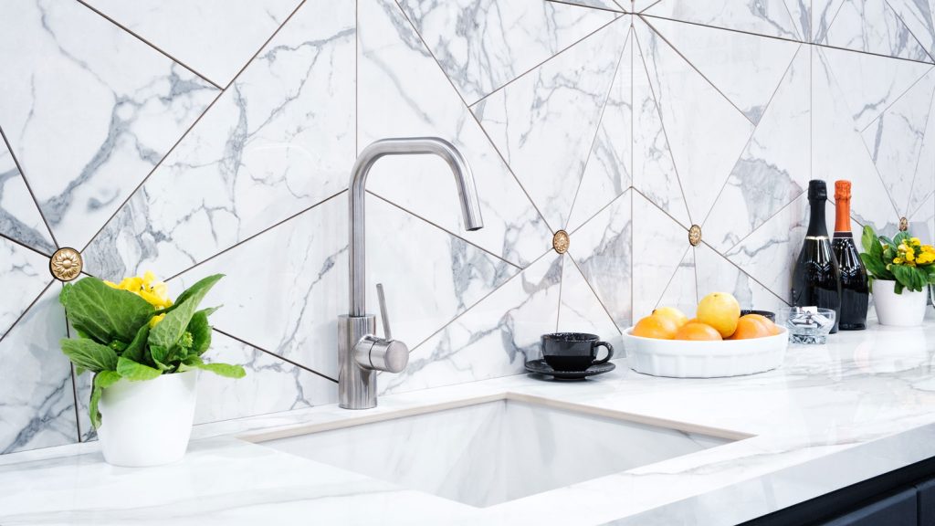 The interior of the modern kitchen is illuminated with a gray stone countertop with a luxury washbasin and mixer, fruit orange and flowers, a bottle with red wine, champagne and chocolate