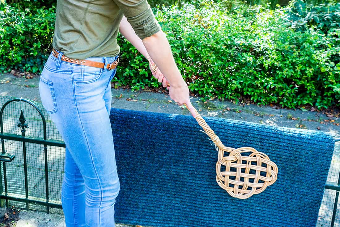 Young caucasian woman beating door mat with carpet beater outside
