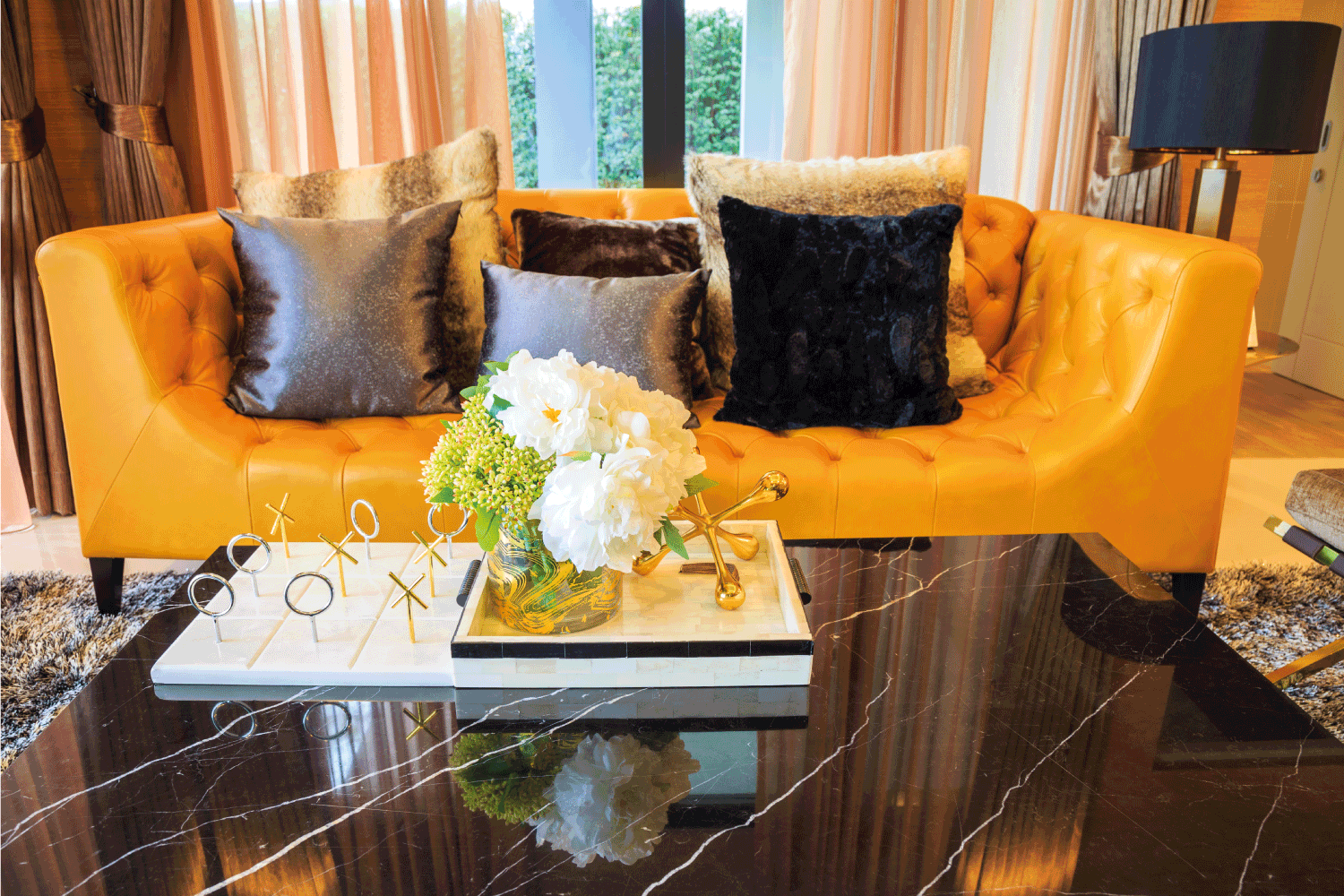 artificial flowers in a pot on a black marble table and pillows on a amber sofa with a lamp and curtain. swept angled track sofa arm