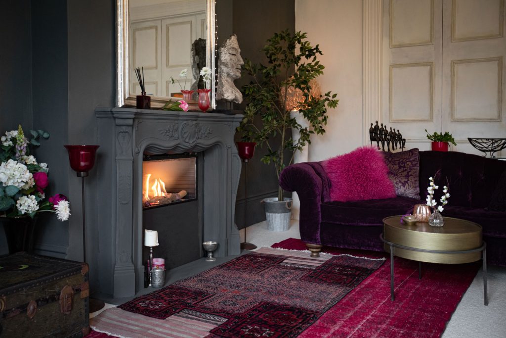 A burgundy carpet in front of the fireplace with gray painted mantel and flowers for decoration