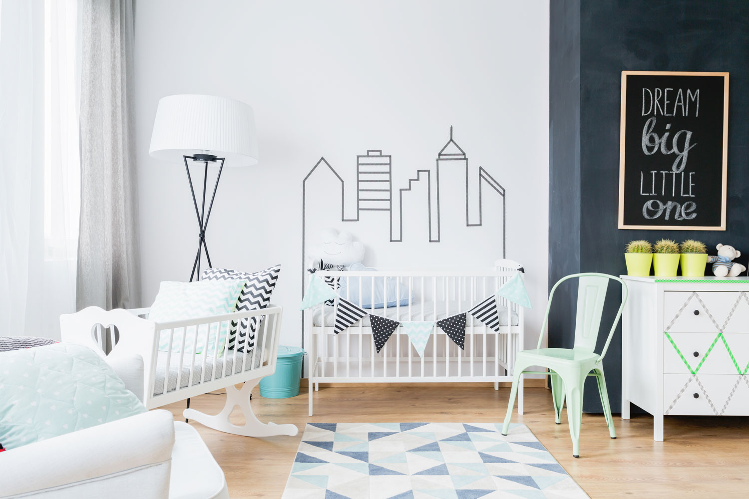 A city scape decorated wall with a white babies crib and small rocking chair