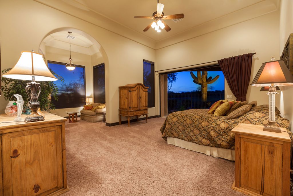 A luxurious master bedroom with burgundy carpet, wooden cabinets and beige colored walls