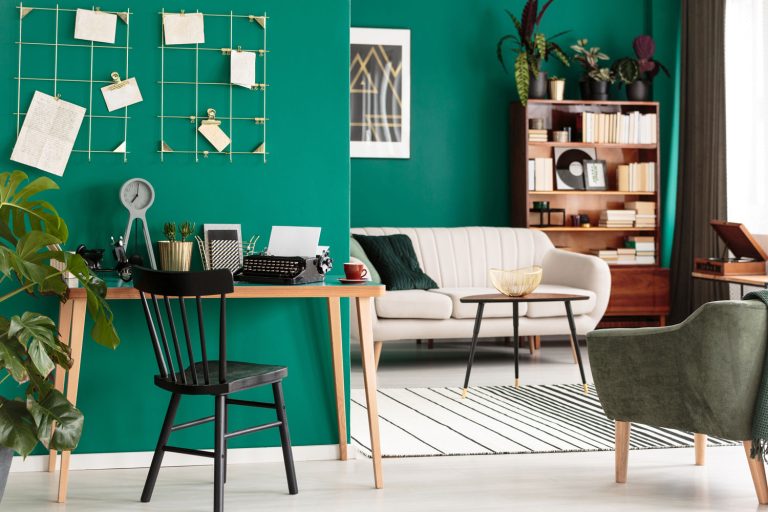 Black chair at wooden desk in green open space interior with armchair and couch, What Colors Tone Down Green Walls? [11 Color Options]