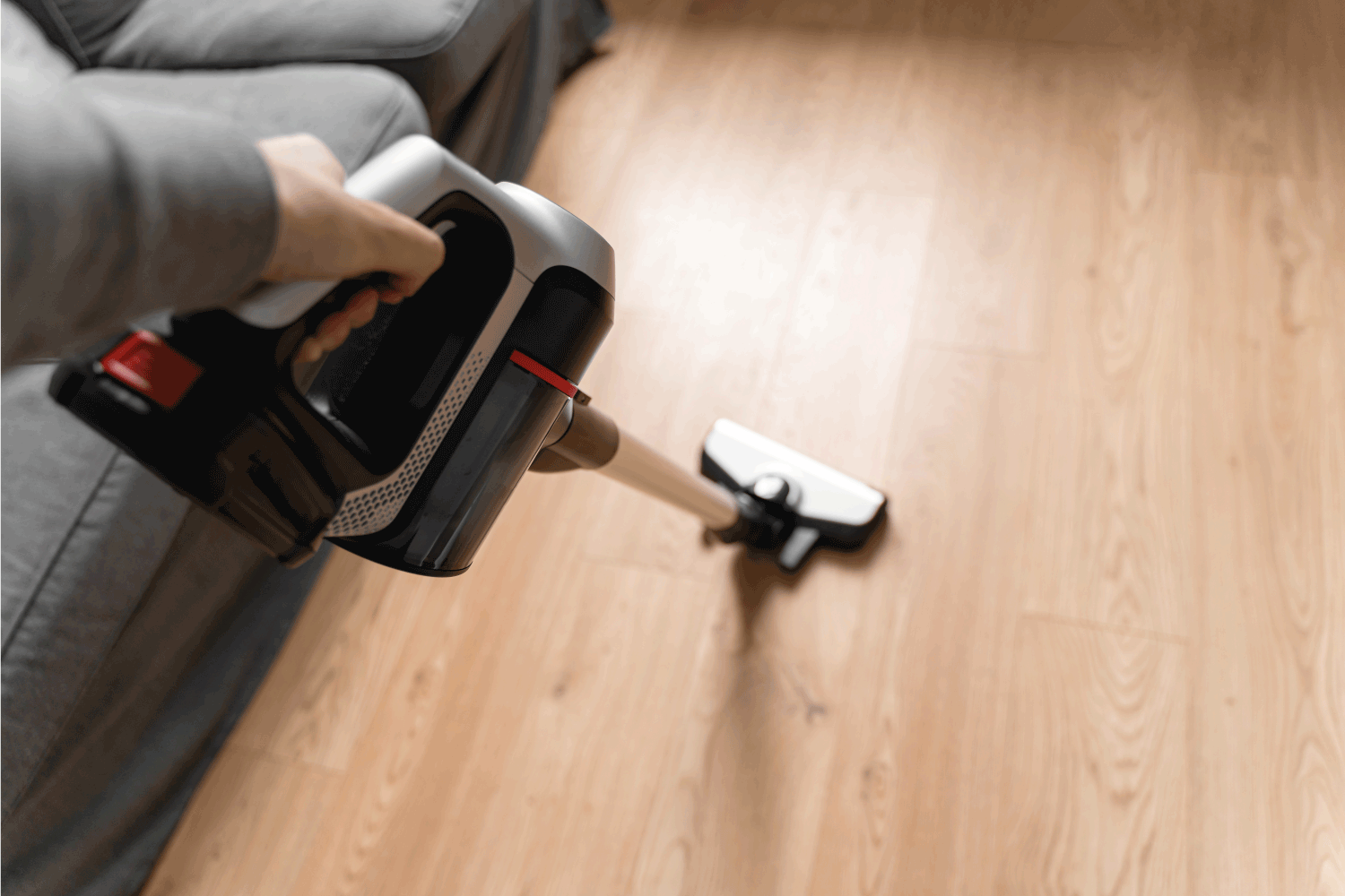 Cleaning wooden floor with wireless vacuum cleaner. Handheld cordless cleaner