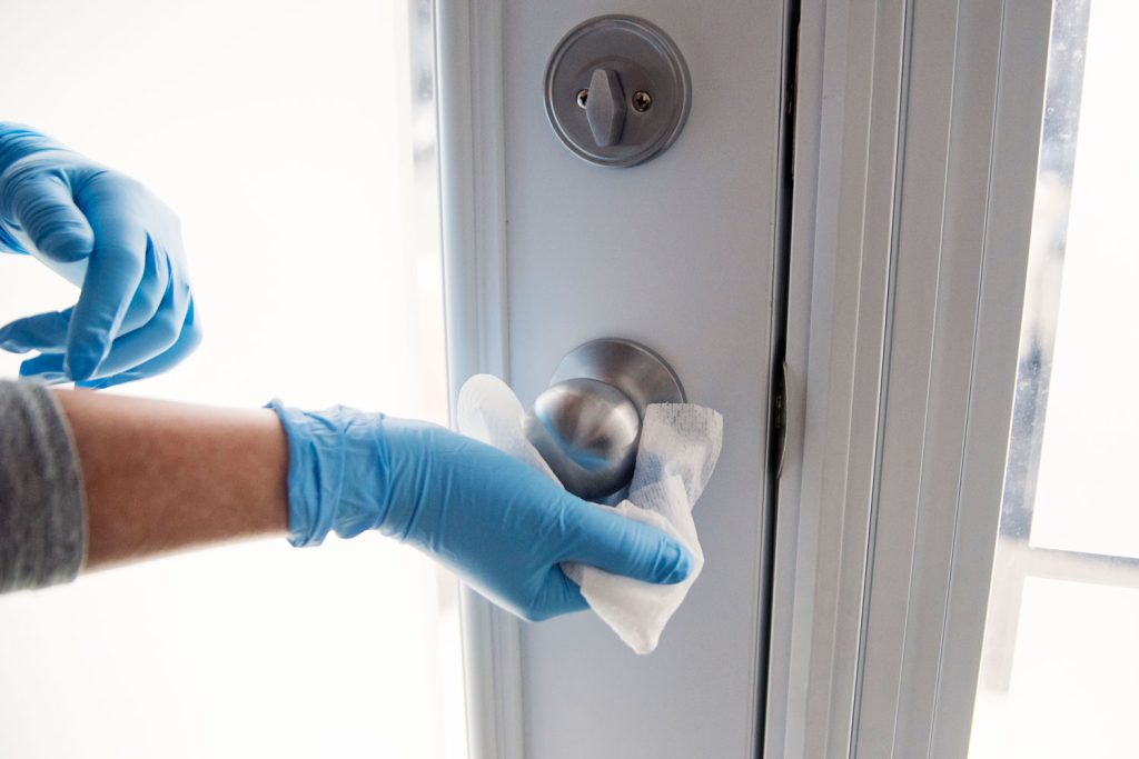 Female hands with blue glove wiping doorknob with disinfectant wipe. 