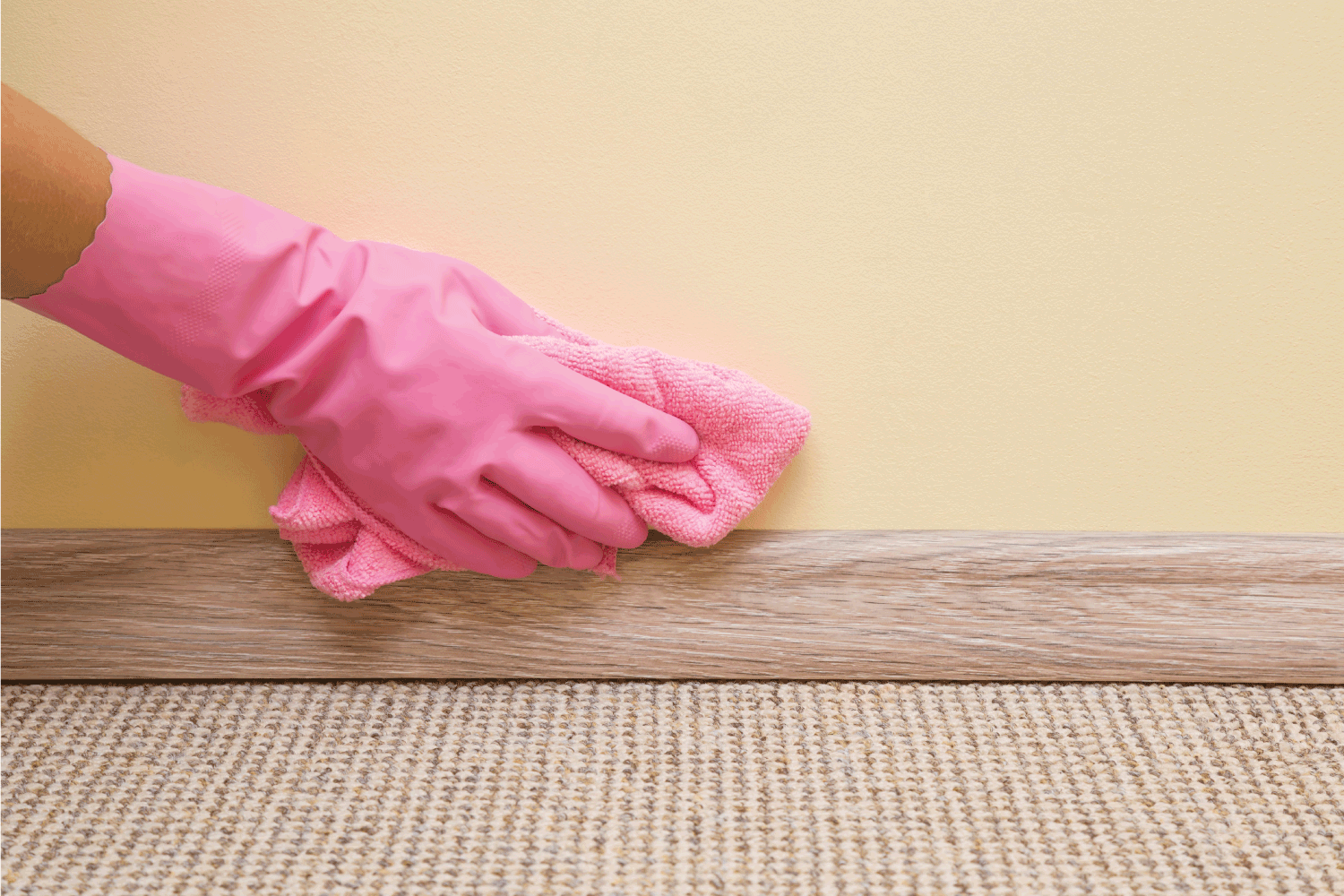 Hand in rubber protective glove with microfiber cloth cleaning baseboard on the floor from dust at the wall