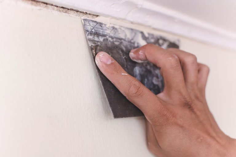 A handyman applies putty or filler to cover the gap between a wood cornice and a concrete wall with a trowel, How To Fix Holes In Plywood Walls