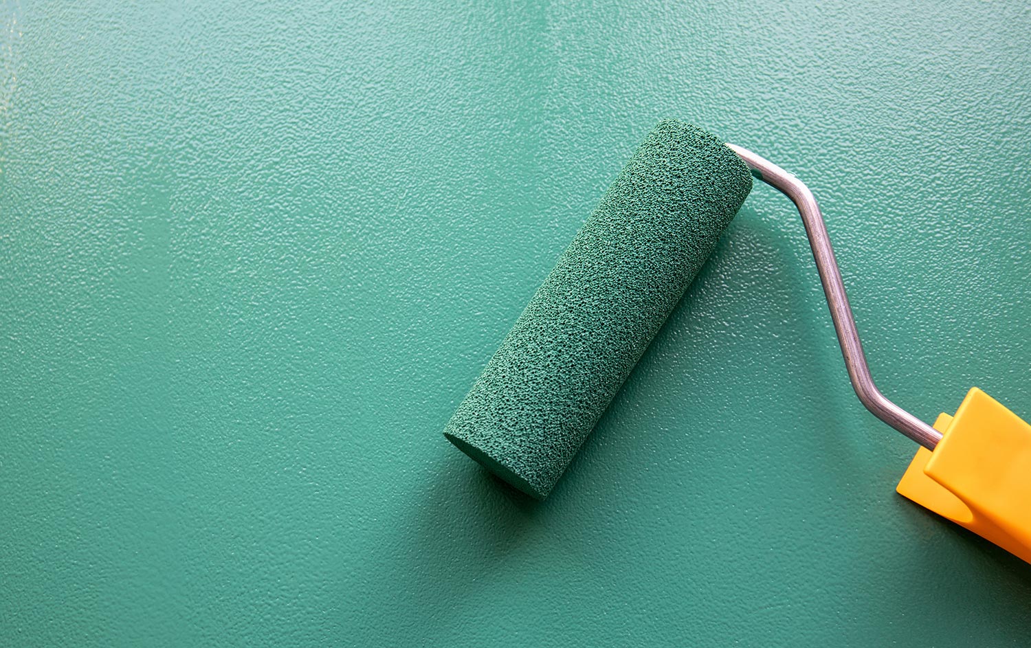 Paint roller with green colour on painted wooden surface