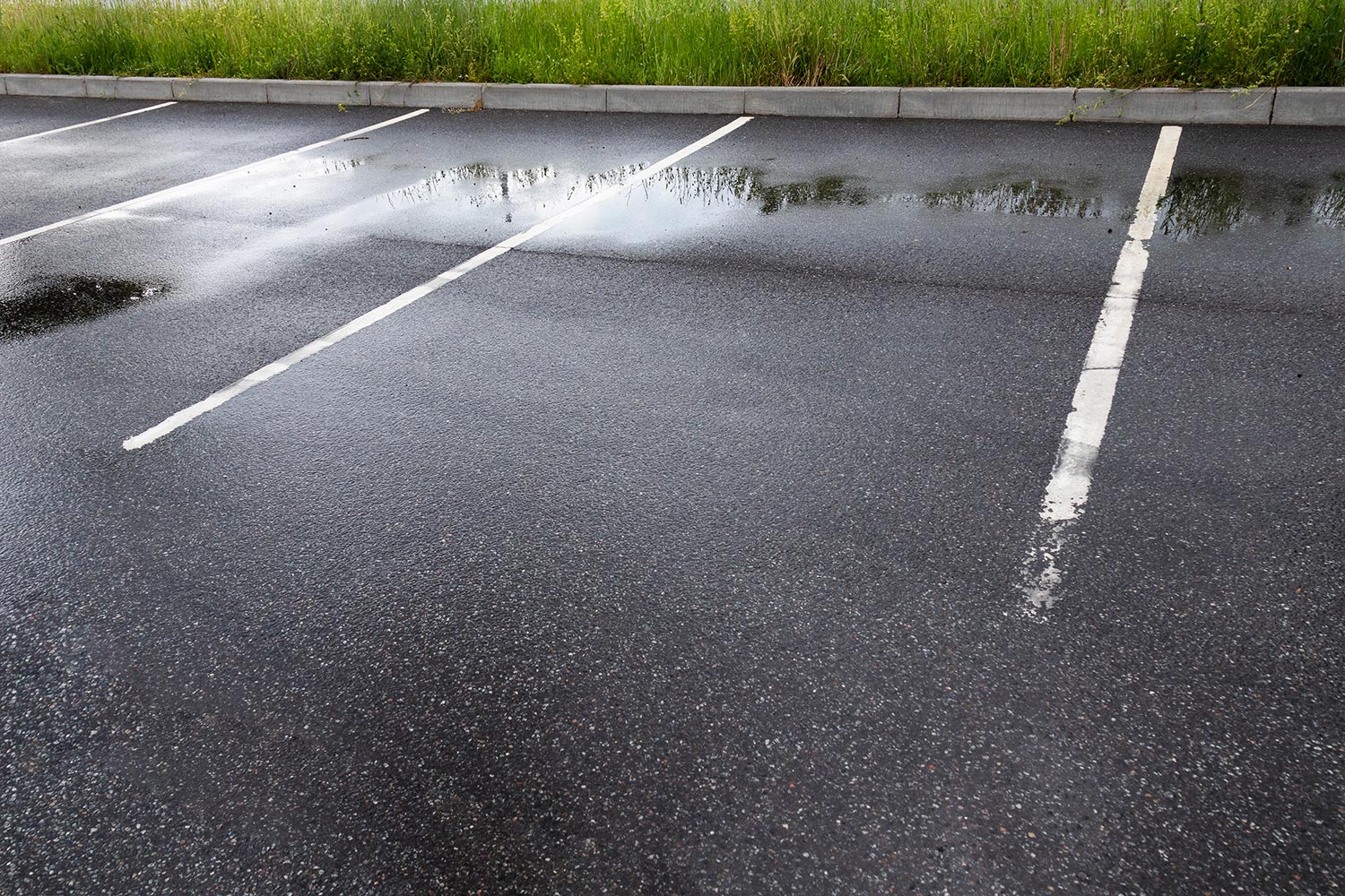 Parking spaces on wet gray asphalt with puddles
