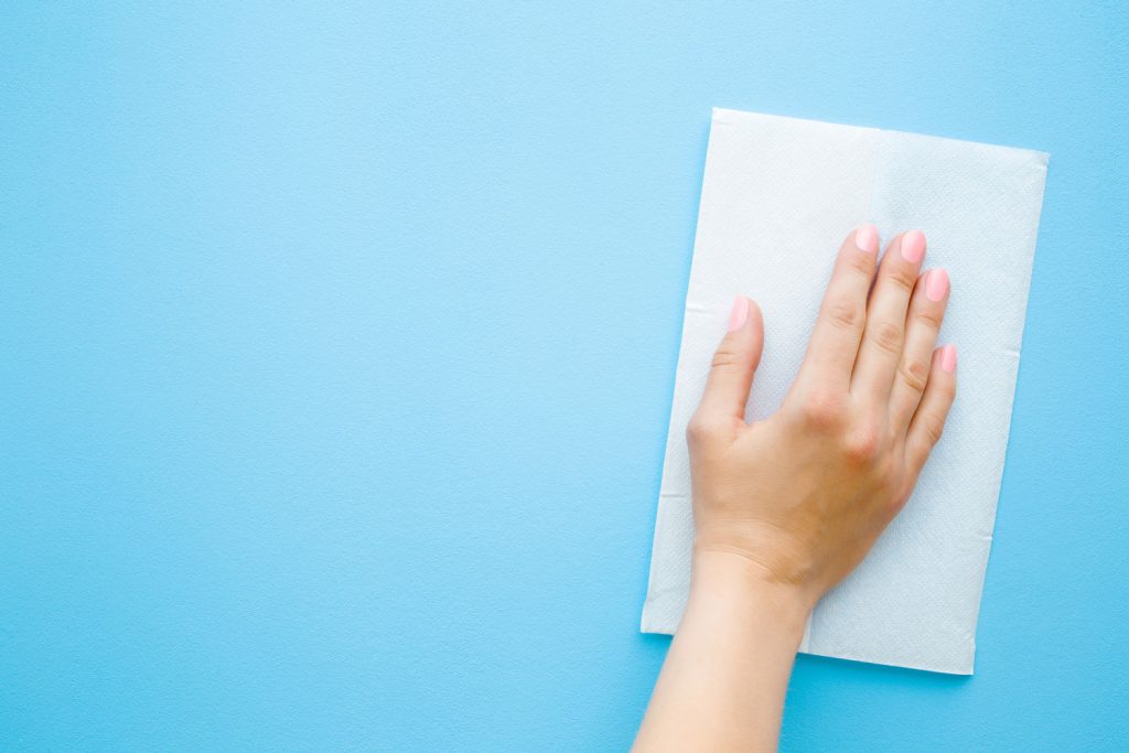 Woman's hand wiping pastel blue desk with white paper napkin