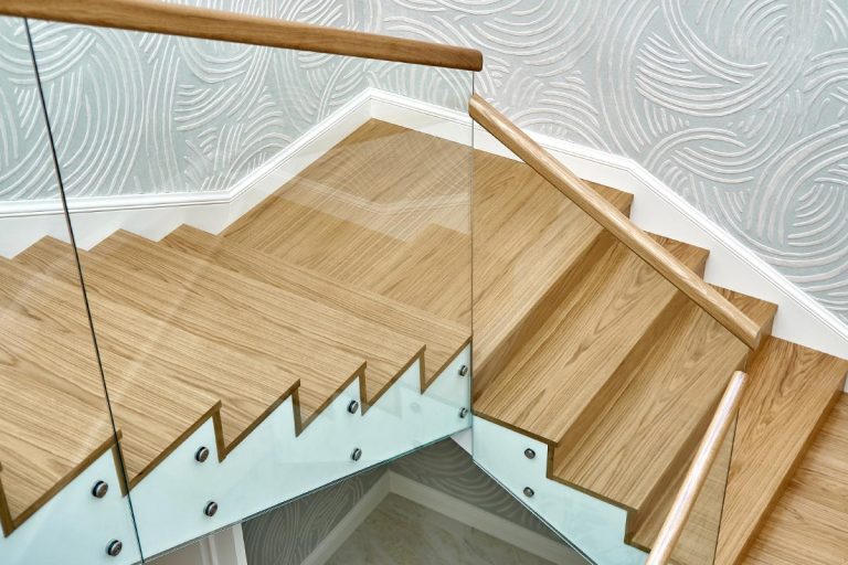 A wooden staircase with glass railings and wooden handrail, How To Fix The Gap Between Stairs And Walls?
