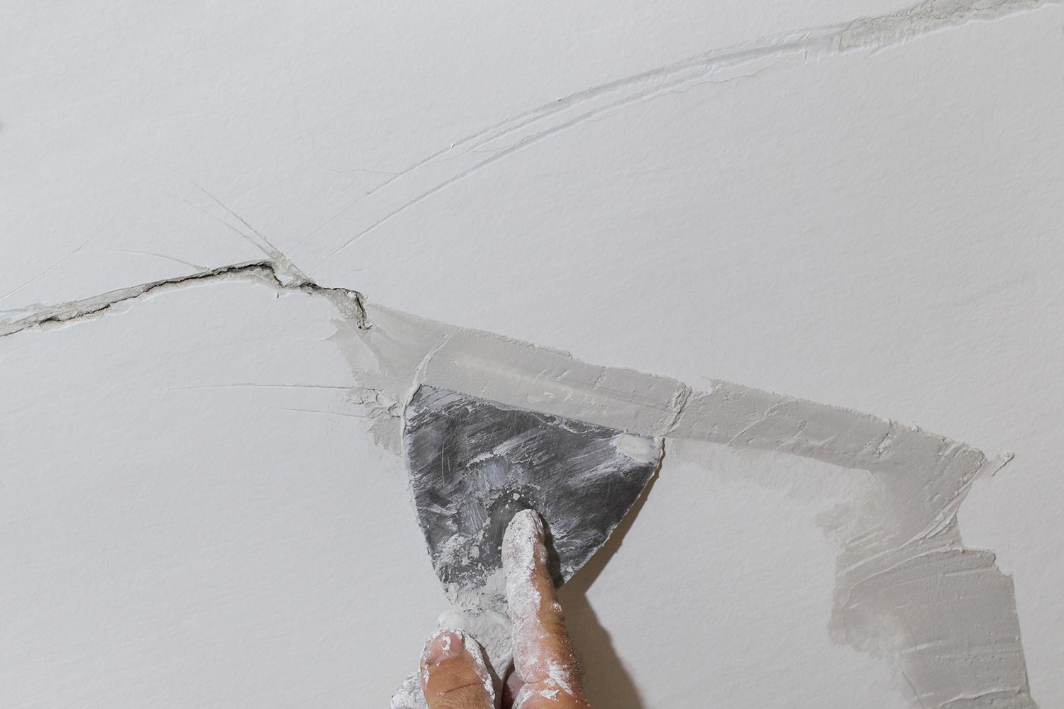 Worker fixing cracks on ceiling spreading plaster using trowel