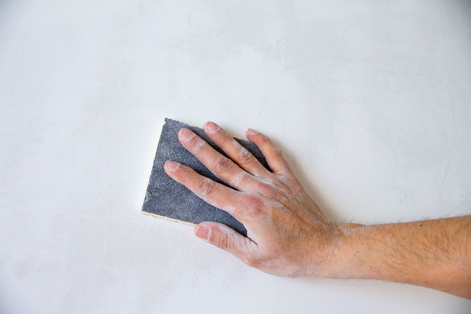 Worker sanding the concrete wall with a sanding paper