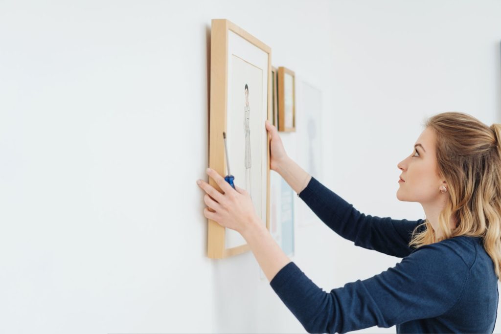 Young attractive blond woman hanging a picture in a plain wooden frame on a wall