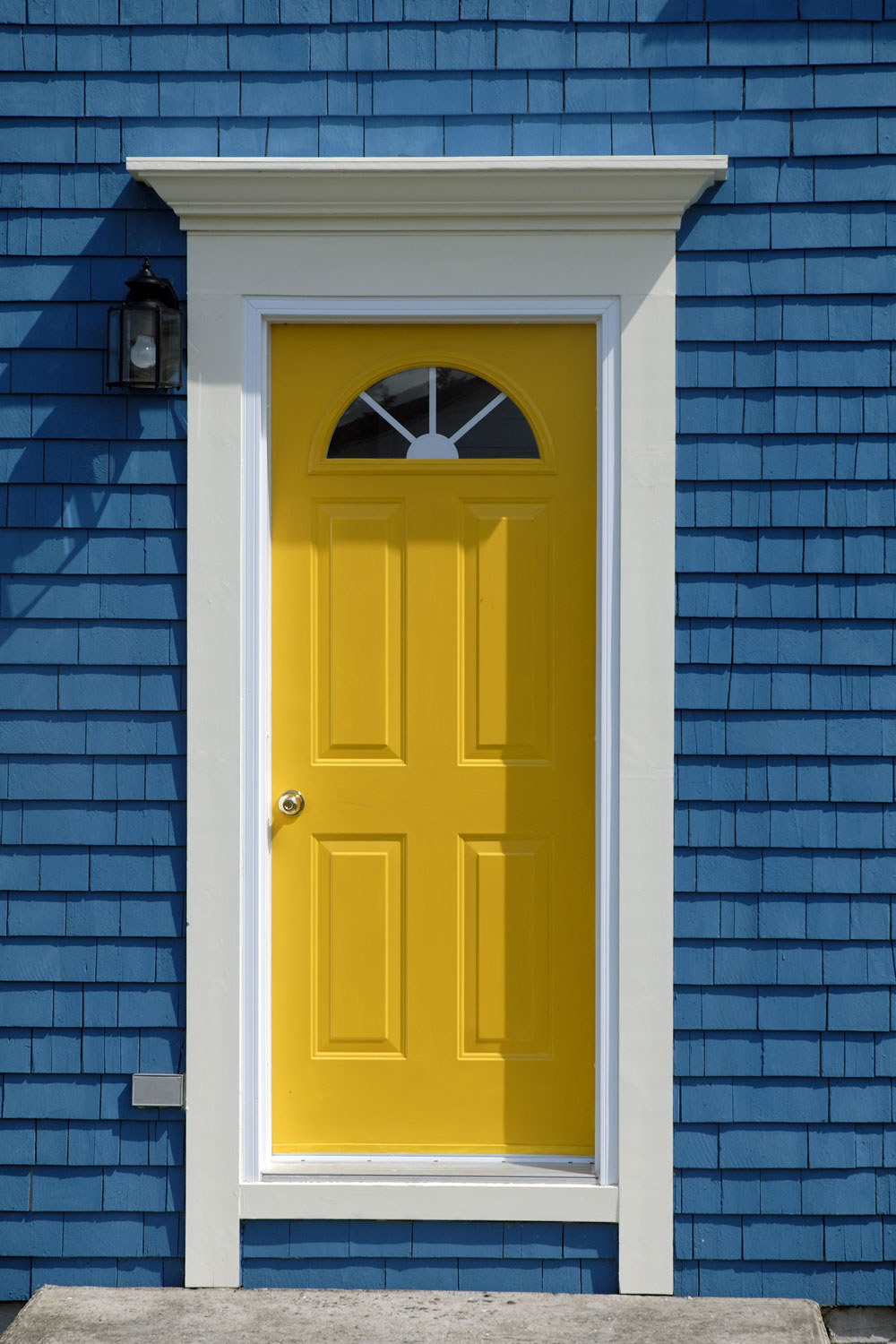 A blue front facade of a classic house with a yellow door and white trims