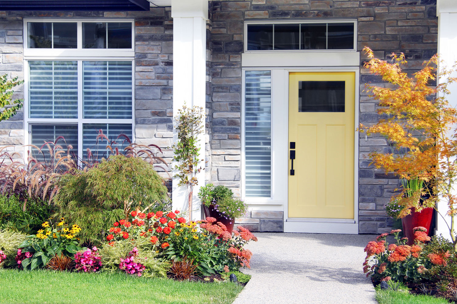 Шикарная лужайка современного дома с цветками и желтой входной дверью