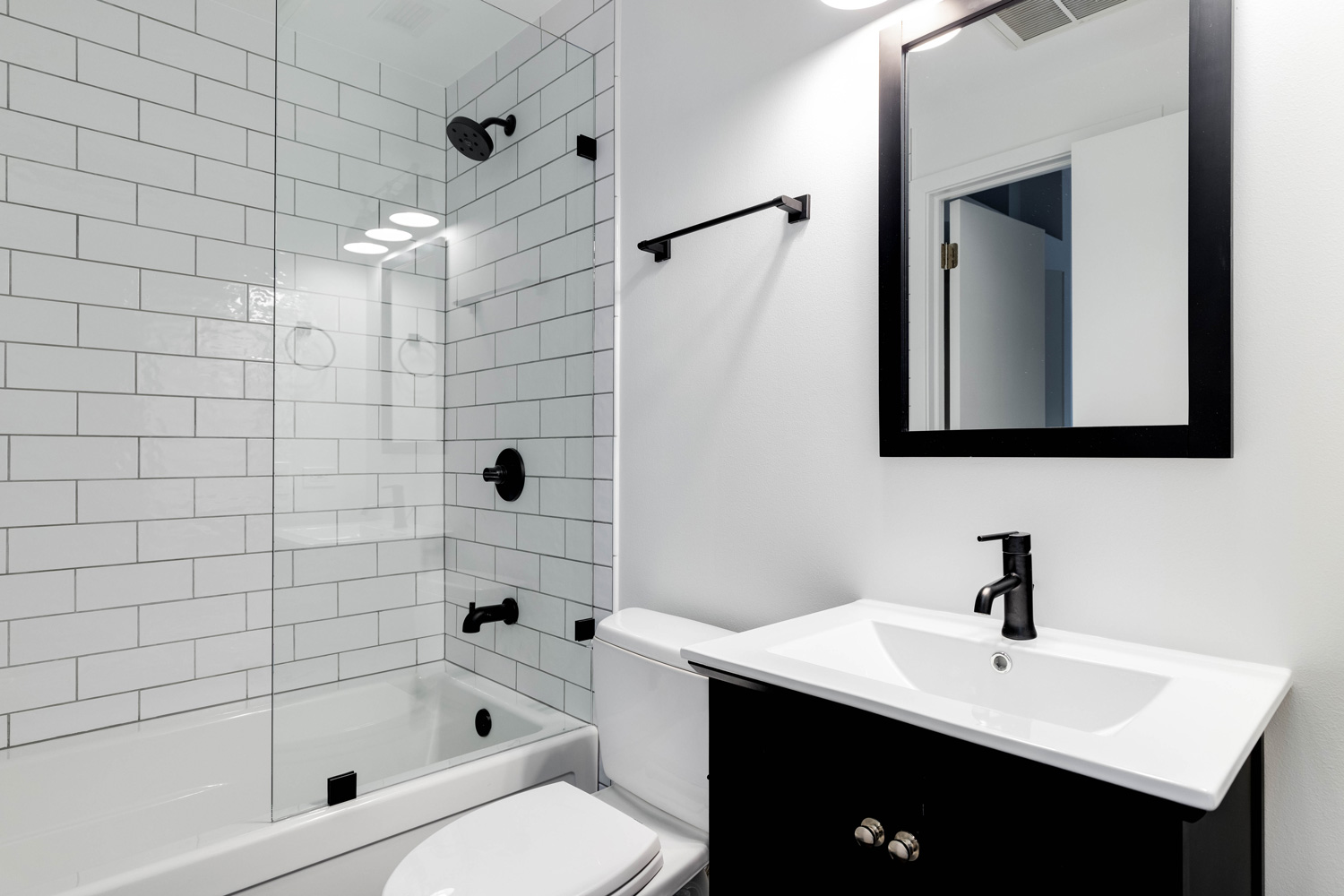 A small modern bathroom with a dark vanity, mirror frame, and hardware.