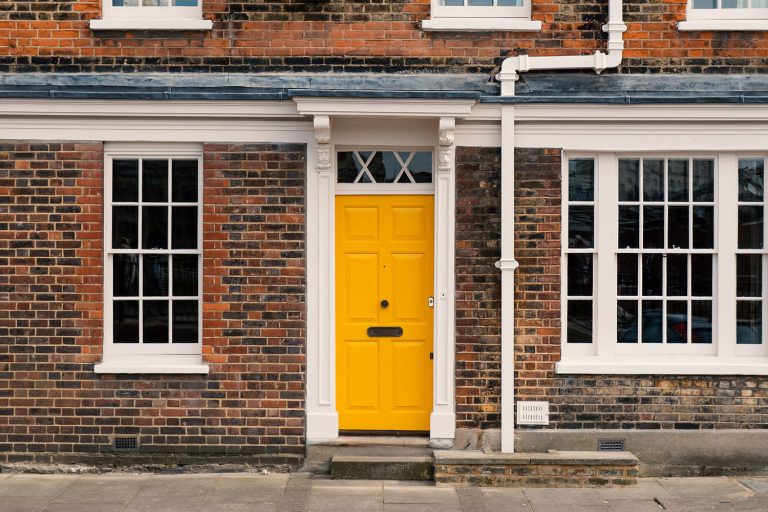 A yellow front door with white trims and a brick facade, What Does A Yellow Front Door Mean?