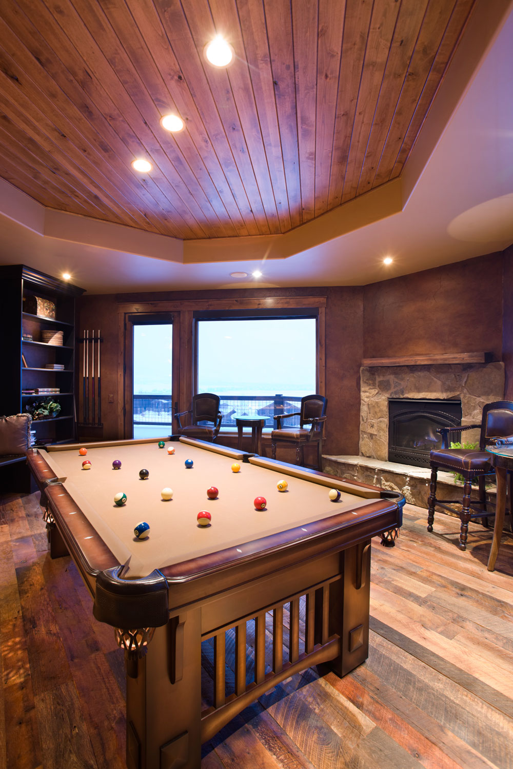 An expensive rustic entertainment room made from wooden paneling, hardwood flooring and an expensive wooden billiard table