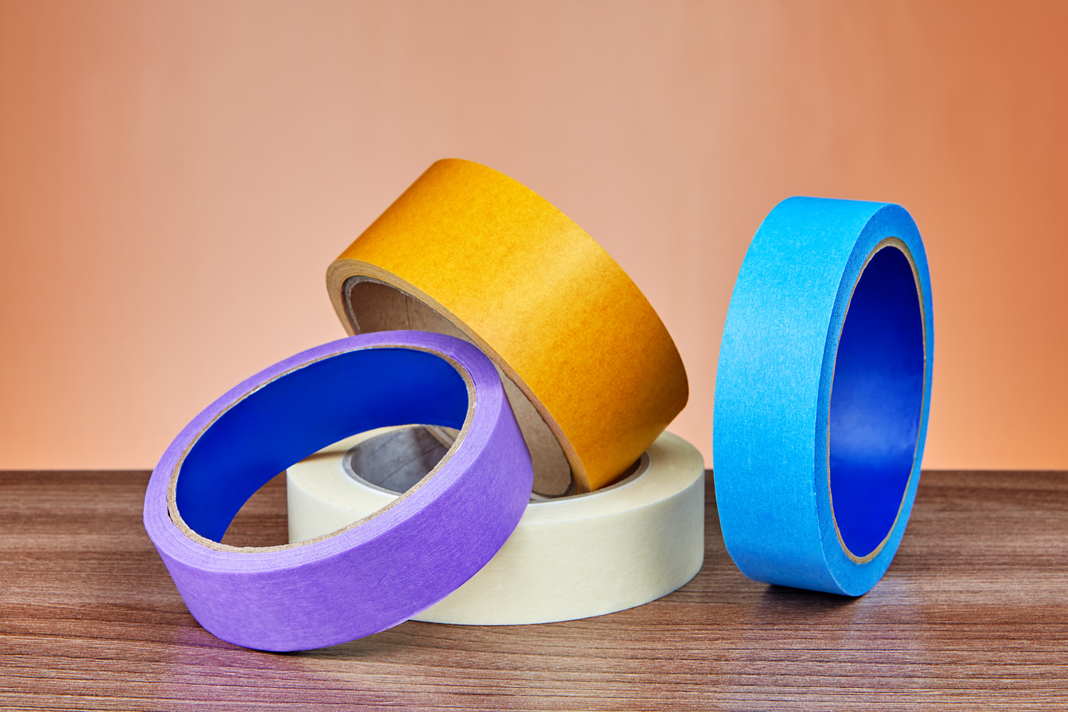 Four multicolored rolls of adhesive tape for various purposes lie on table.
