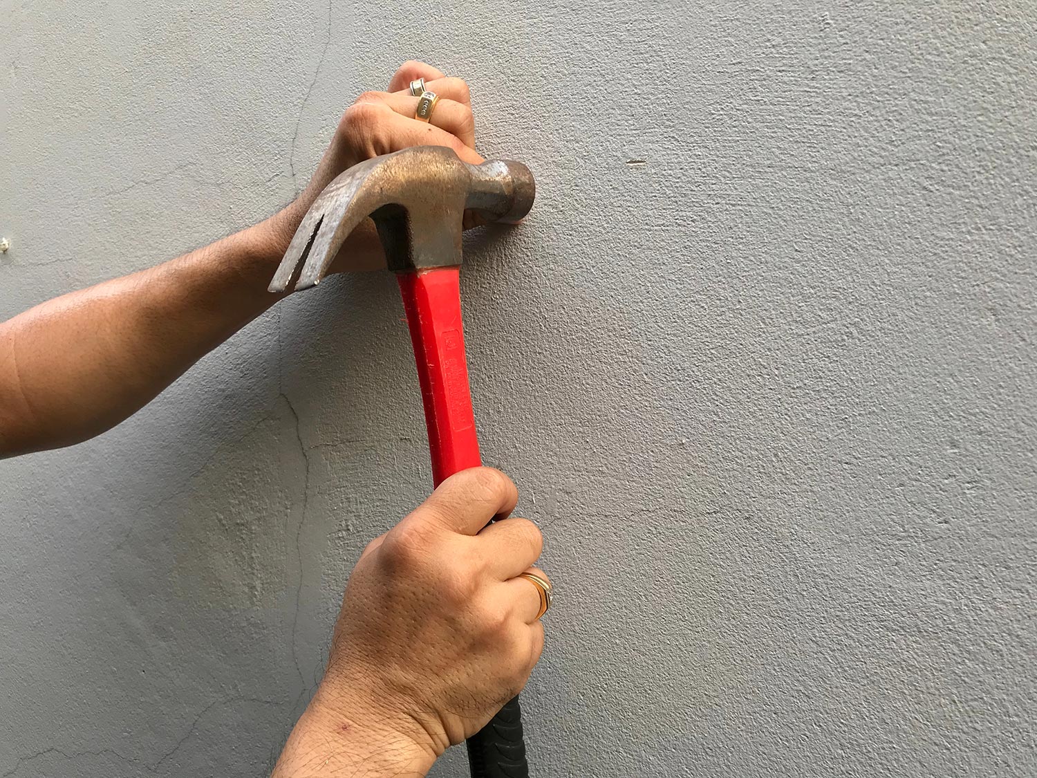 Man hitting nail on cement wall, red hammer for craft work