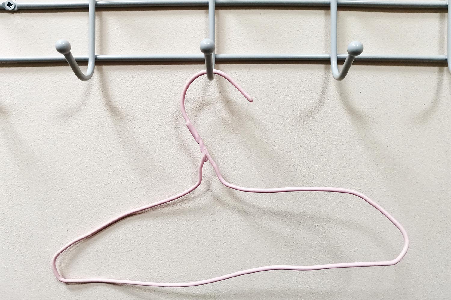 Pink curved old clothes hanger hanging on a hook