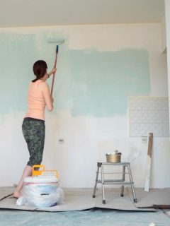 A woman painting wall using paint roller, How Much Does It Cost To Paint Basement Walls?