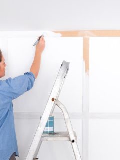 Woman painting wood panelled wall with white primer paint while standing on a ladder, Does Primer Need To Be Even?