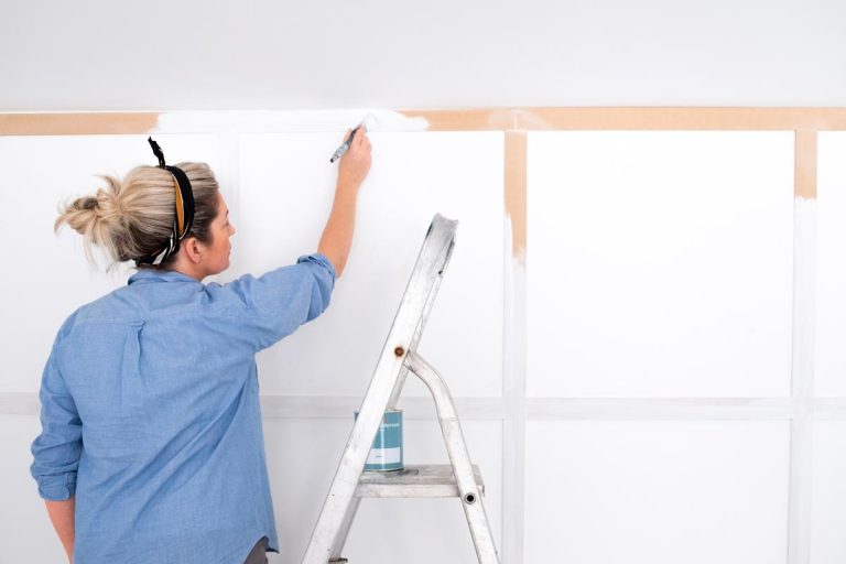 Woman painting wood panelled wall with white primer paint while standing on a ladder, Does Primer Need To Be Even?
