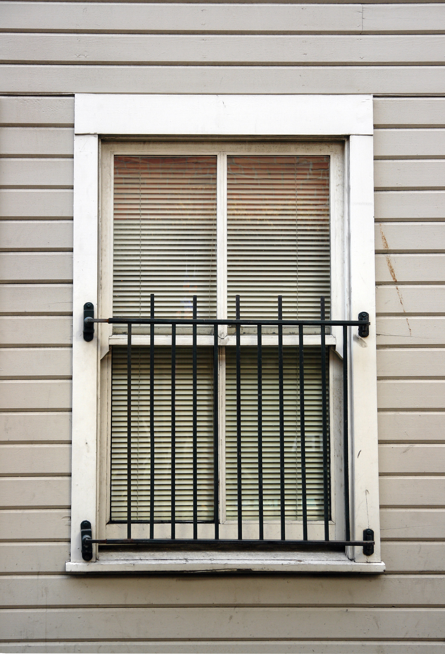 A double-hung window with a wrought-iron grate looks upon an urban alley.