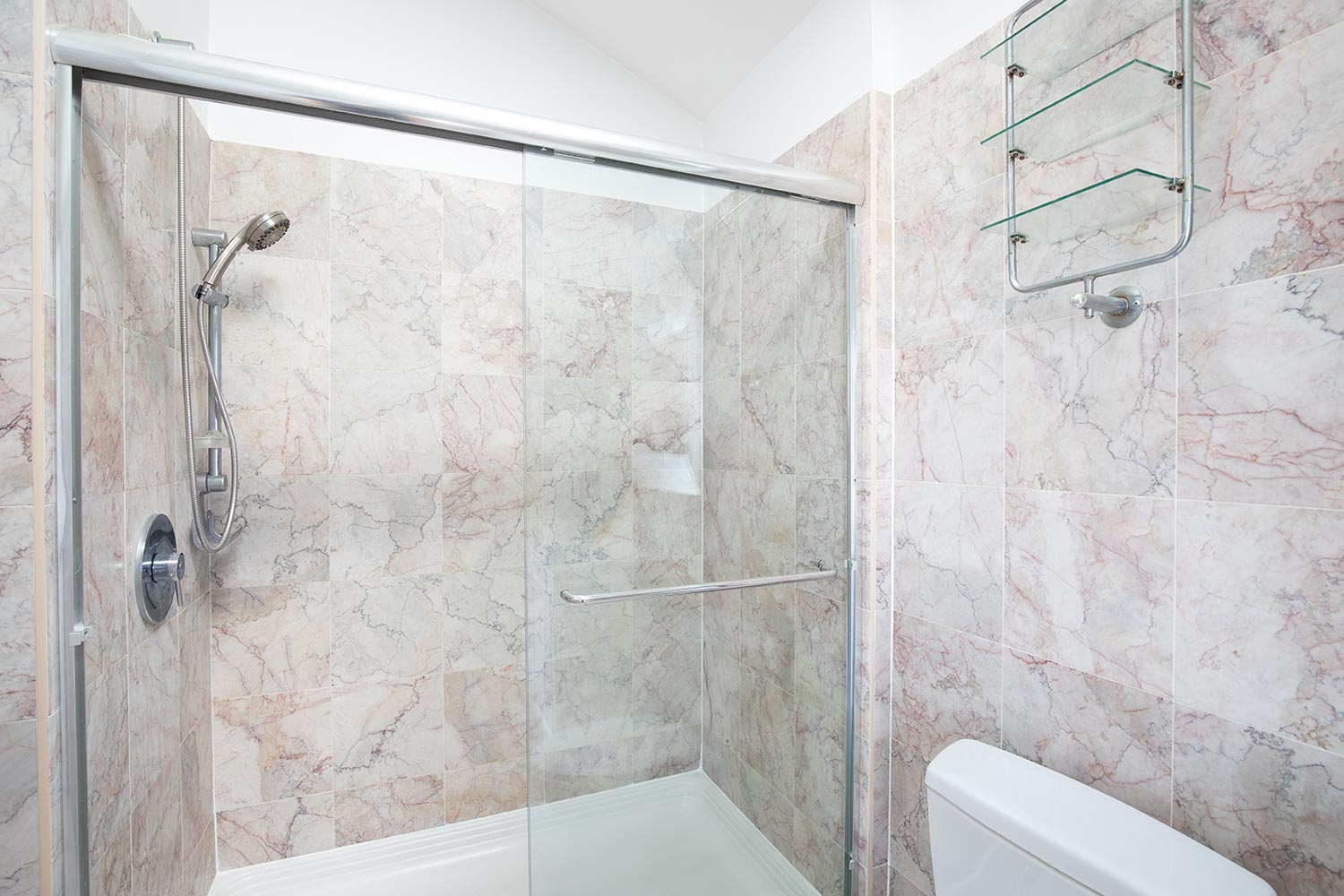 A marble tiled shower with a glass sliding door and chrome hardware