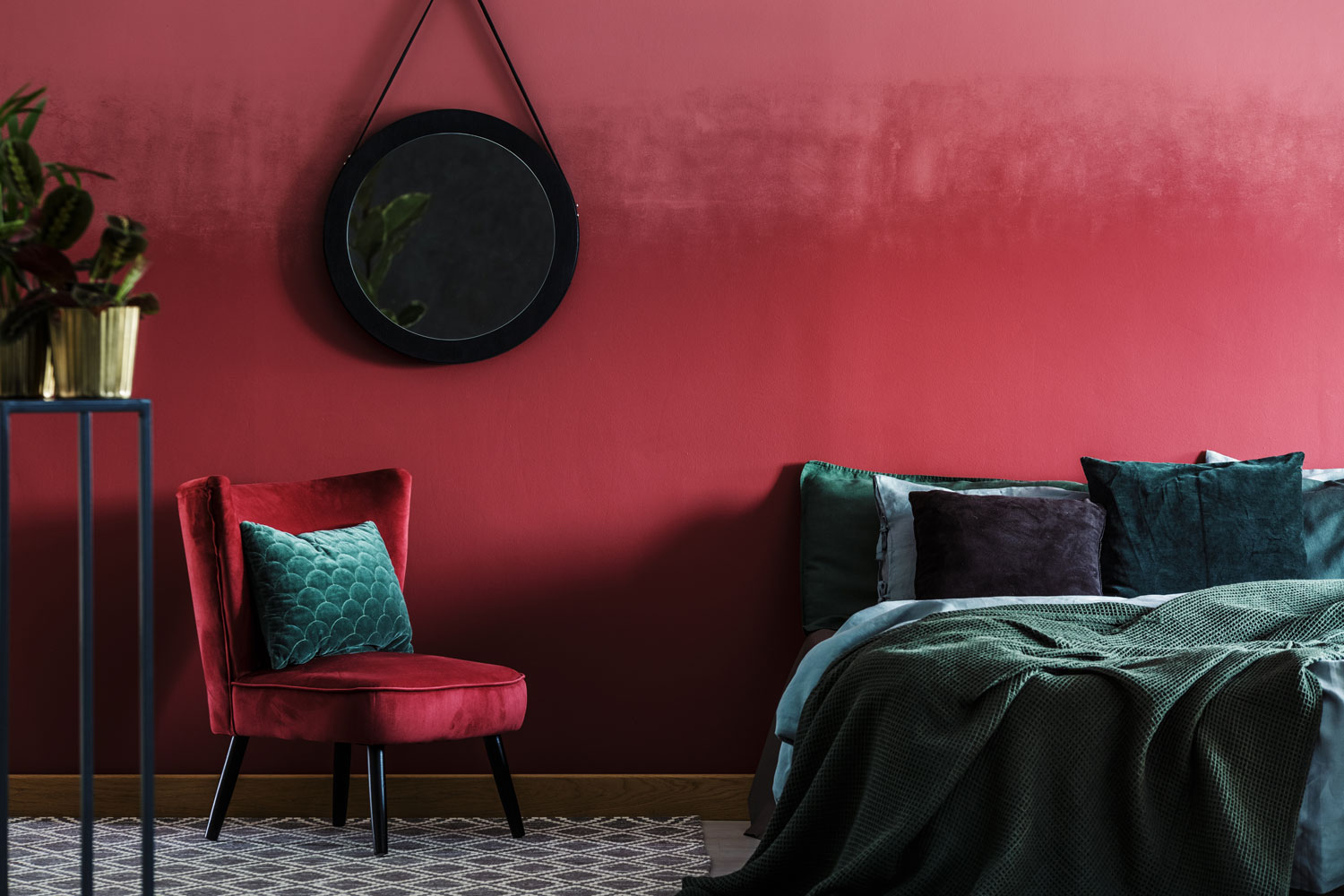 A red velvety bedroom with green beddings and a small red chair on the side